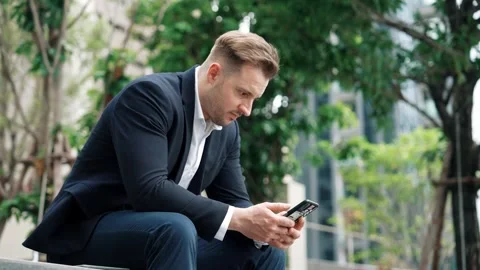 Businessman sitting at park while working on phone by reading report. Urbane Stock Footage 265030600