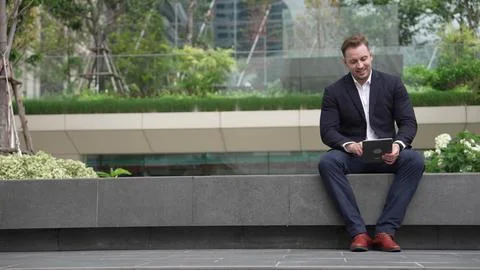 Businessman sitting at park while working on tablet by reading report. Urbane Stock Photos