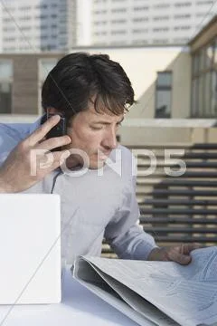 A businessman sitting on a rooftop terrace with a newspaper, mobile phone and Stock Photos