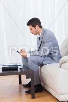 Businessman sitting on sofa texting message with his mobile Stock Photos