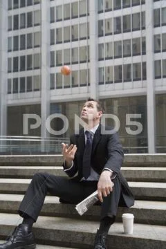 Businessman sitting on steps during coffee break and tossing apple in the air Stock Photos