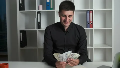 Businessman sitting at a table counts dollars and happily scatters money around Stock Footage 133569274