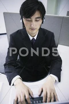 Businessman sitting working on a laptop wearing headphones Stock Photos