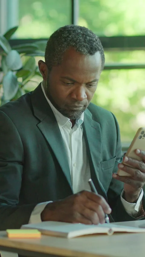 A businessman skillfully engaged in dual tasking, managing both a smartphone and Stock Footage 314208949