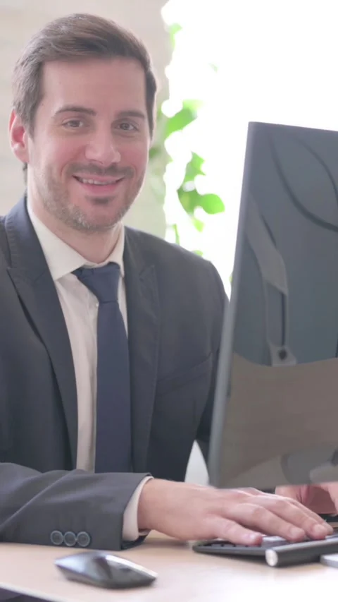 Businessman Smiling at Camera while Using Desktop Computer, vertical video Stock Footage 328977533