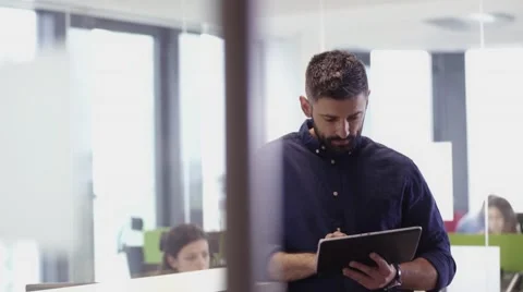Businessman smiling to camera whilst using tablet in the office 스톡 동영상 67345802
