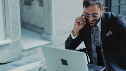 Businessman smiling, talking on the phone while working on laptop 스톡 동영상 96297585