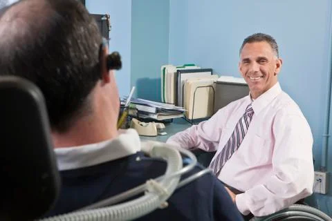 Businessman with spinal cord injury talking to his colleague  with Duchenne m Stock Photos