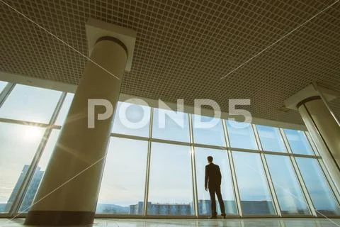 The businessman stand near panoramic window on the sunset background Stock Photos