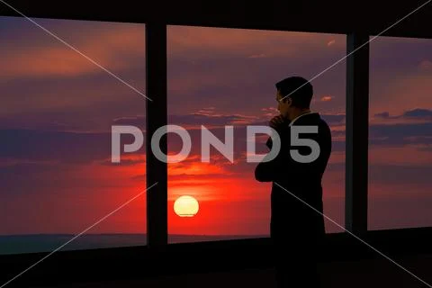 The businessman stand near the panoramic window. Evening night time Stock Photos
