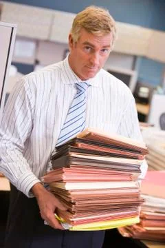Businessman standing in cubicle with stacks of files Stock Photos