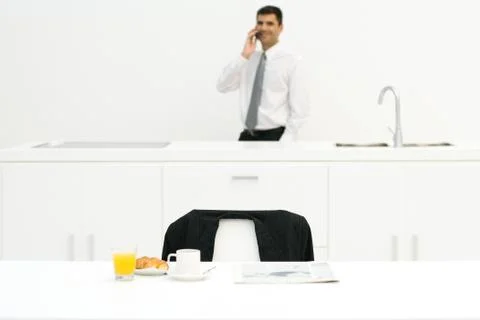 Businessman standing in kitchen, using cell phone, focus on breakfast in Stock Photos