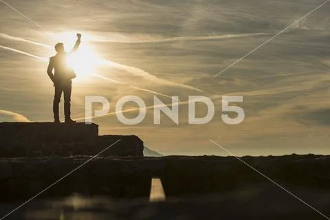 Businessman standing outdoors on a wall with his fist raised against a sun Stock Photos