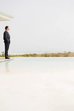 Businessman standing at the poolside and looking at sea view Stock Photos