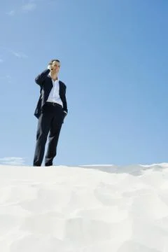 Businessman standing on sand, using cell phone, low angle view Stock Photos