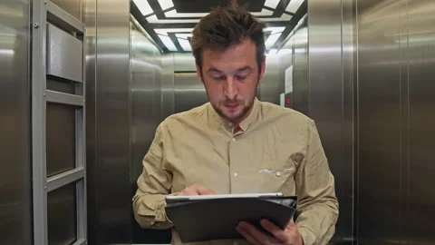 A businessman studies documents while riding in the elevator of business center 스톡 동영상 245692874