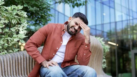 Businessman is suffering from headache while sitting on bench near modern office Video stock 315559845