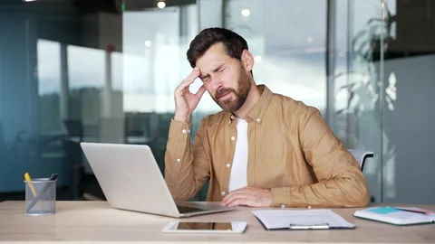 Businessman suffering from headache while working on laptop while sitting  Stock Footage 295042955