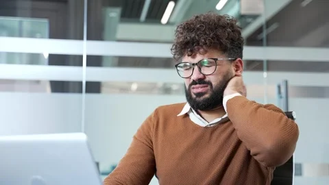 Businessman suffering from neck pain while working on laptop sitting at desk  Stock Footage 333119294