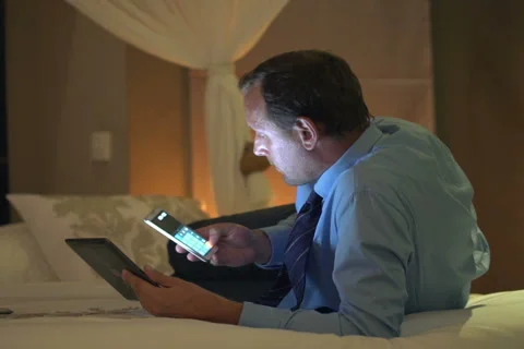 Businessman with tablet computer calculating data on smartphone lying on bedNTSC Stock Footage 45443618