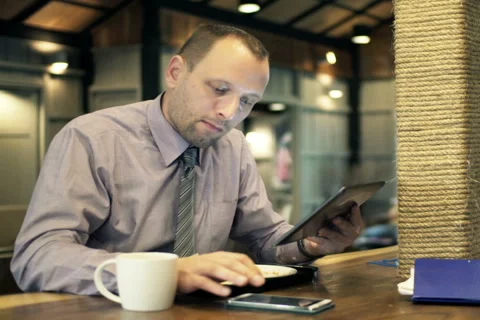 Businessman with tablet computer calculating data on smartphone in cafe NTSC Stock Footage 49699986