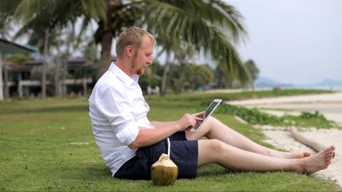 Businessman with a tablet tablet and drinks coconut on the beach 스톡 동영상 88281123