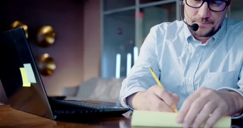 Businessman Taking Notes in Office Video Call Stockbeeldmateriaal 323680375