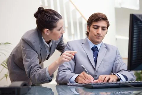 Businessman taking notes while getting explanation by colleague Stock Photos