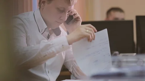 Businessman talking on mobile phone and looking at documents on desk Video stock 89669341