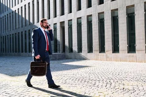 Businessman talking to the mobile while walking in the street Stock Photos