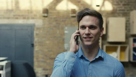 Businessman talking on phone while her colleagues walk around office Stock Footage 107890326