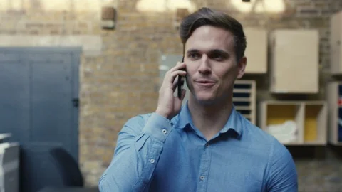 Businessman talking on phone while her colleagues walk around office Stock Footage 107890359