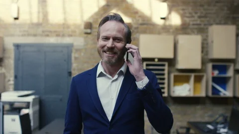 Businessman talking on phone while her colleagues walk around office Stock Footage 107890570