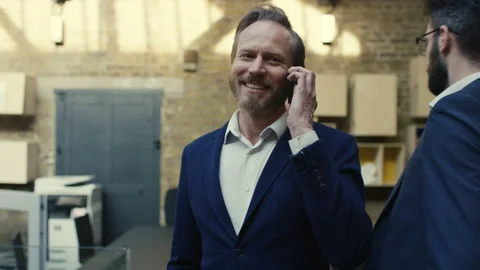 Businessman talking on phone while her colleagues walk around office Stock Footage 107890656