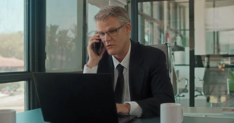 A businessman talking on the phone while working on a laptop at the office. Stock Footage 140183316