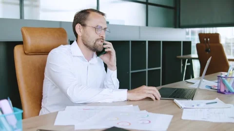 Businessman talking on phone while working with laptop at desk in modern office Stock Footage 315762038