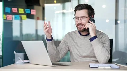 Businessman talking on smartphone while sitting at desk at workplace in modern  Stock Footage 331378627