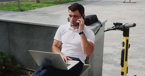 Businessman talking on smartphone while using laptop at park in city Video stock 285205025