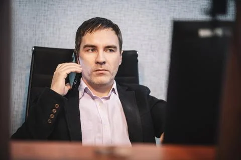 Businessman talking on smartphone while working at computer in modern office. Stock Photos