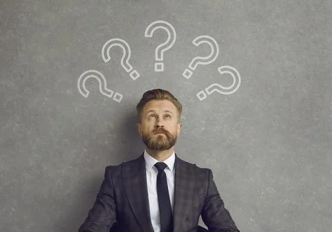 Businessman thinking of answer looking up at several question marks above his Foto stock