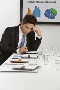 Businessman touching his forehead while writing Stock Photos