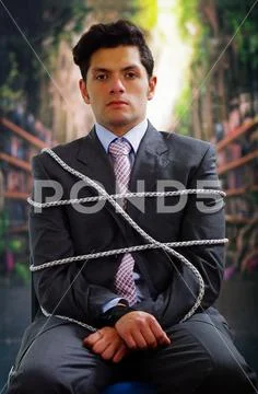 Businessman trapped in a chair with rope in a blurred background Stock Photos