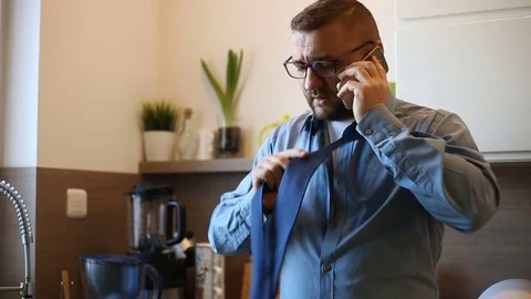 Businessman trying to tie the necktie while quarrelling on cellphone Stock Footage 73504142