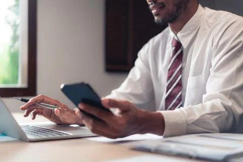 Businessman type data on laptop while checking report on smartphone and ana.. Stock Photos