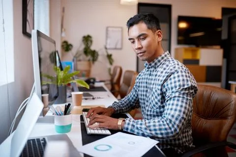 A businessman types on his computer while looking at printed report Stock-Fotos