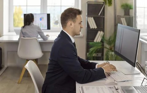 Businessman typing at desktop computer in bright office with coworker in Stock Photos