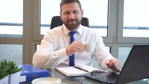 Businessman typing on laptop computer, drinks coffee and smiles at camera Vídeos de archivo 72499936