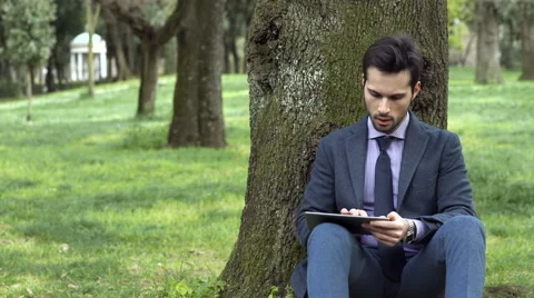 Businessman under a tree working with his tablet Stock Footage 64734396