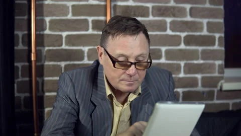 Businessman uses a digital tablet in a room with a brick wall. Stock Footage 87733434