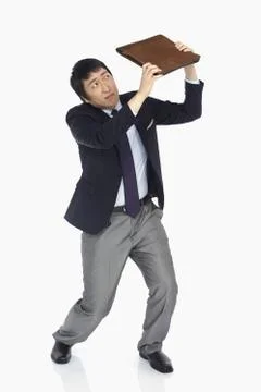 Businessman using a briefcase to shield himself Stock Photos